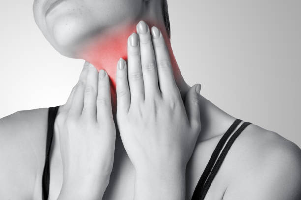 Closeup view of a young woman with pain on neck or thyroid gland on gray background. Closeup view of a young woman with pain on neck or thyroid gland on gray background. Black and white photo with red dot. dhole stock pictures, royalty-free photos & images