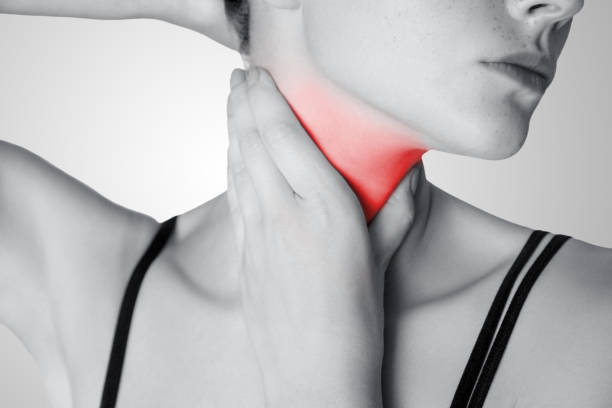Closeup view of a young woman with pain on neck or thyroid gland on gray background. Closeup view of a young woman with pain on neck or thyroid gland on gray background. Black and white photo with red dot. dhole stock pictures, royalty-free photos & images