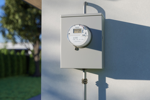 Close-up View Of Electric Meter On Building Facade With Blurred Garden Background