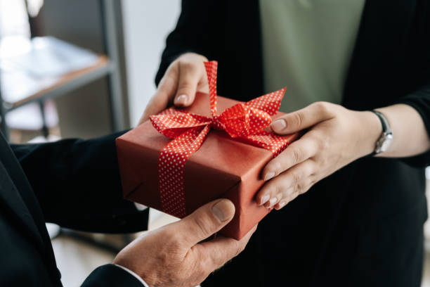 Close-up view of hands of unrecognizable woman giving red gift box tied to bow handed to man. stock photo
