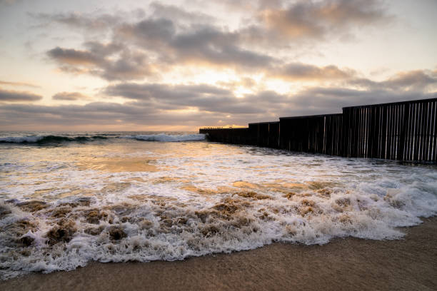 вид крупным планом на пляж и волны на закате возле международной пограничной стены в playas tijuana, мексика - tijuana стоковые фото и изображения