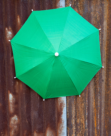 A close-up view of the top background of a large green tarpaulin umbrella mounted against an old galvanized wall covered with brown iron rust.