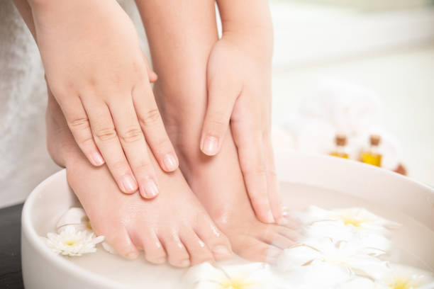 closeup view of woman soaking her hand and feet in dish with water and flowers on wooden floor. Spa treatment and product for female feet and hand spa. white flowers in ceramic bowl. stock photo