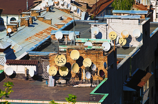 Close-up view roofs of residential buildings. A lot of funny decorated satellite antennas on the house's roof. View of the famous Podil neighborhood in Kyiv, Ukraine. Sunny spring day.