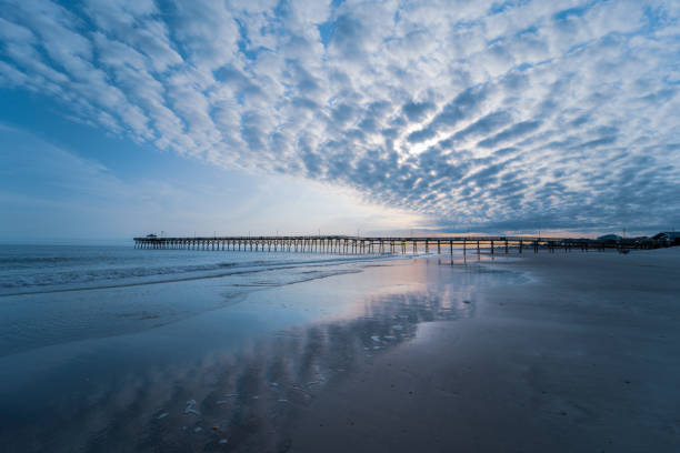 Cloudy Beach Pier Horizon A long beach fishing pier on the horizon with beautiful spattered clouds. north carolina beach stock pictures, royalty-free photos & images