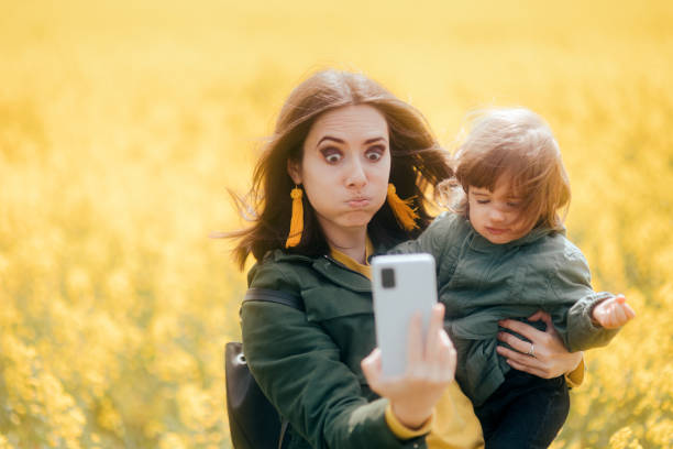 Clumsy Mom and Upset Daughter Taking Selfies in Rapeseed Field Mother trying to take a mobile photo with her child with wind ruing her hair mistake photos stock pictures, royalty-free photos & images