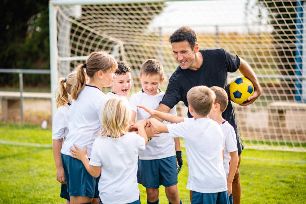 Coach and Young Footballers Showing Unity With Stacked Hands Mature male coach motivating pre-adolescent boy and girl players with stacked hands gesture of team unity. coaching stock pictures, royalty-free photos & images