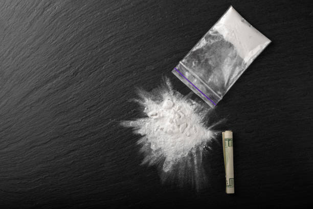 Cocaine in a plastic package on a black background, close-up. A rolled up dollar bill for drug use. Cocaine in a plastic package on a black background, close-up. A rolled up dollar bill for drug use. Prohibited drugs. snorting stock pictures, royalty-free photos & images