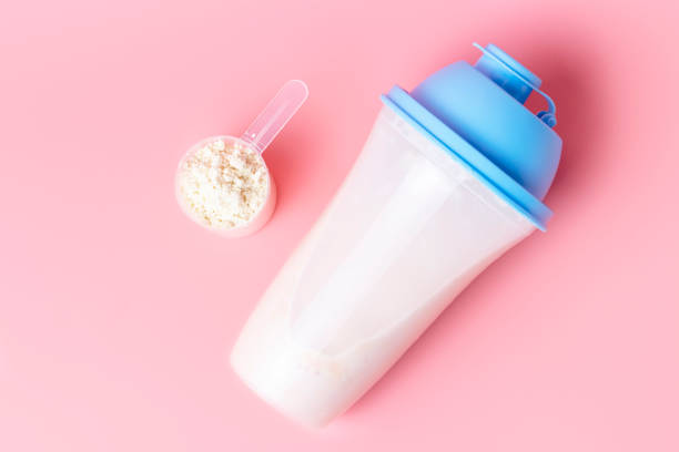 Cocktail shaker and measuring spoon with protein on a pink background, top view. stock photo