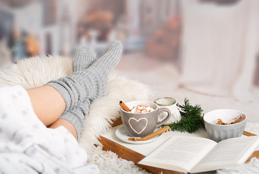 Woman lies with Cup; Kako; Hot chocolate; marshmallows; Book tray; Bed; Sofa; Blanket; Snuggle blanket; Fur; Fireplace; Wind light; Indoor; Living room; Cosy; Reading; Enjoying; Relaxing; Winter time; Autumn time