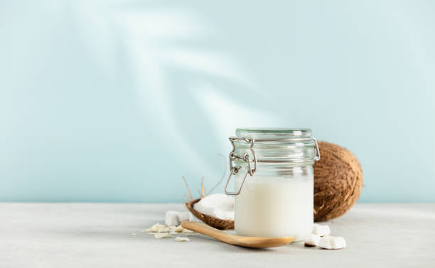 Coconut oil in jar with fresh coconut and tropical leaf shadow, Spa cosmetic and food ingredient stock photo