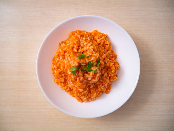 Cod and red tomato rice dish, Italian fish and rice recipe, top view of a white plate Carnaroli rice on wooden table stock photo