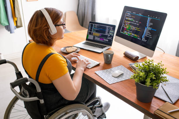 Coding web game at home Female freelance programmer in modern headphones sitting in wheelchair and using computers while coding web game at home disability stock pictures, royalty-free photos & images