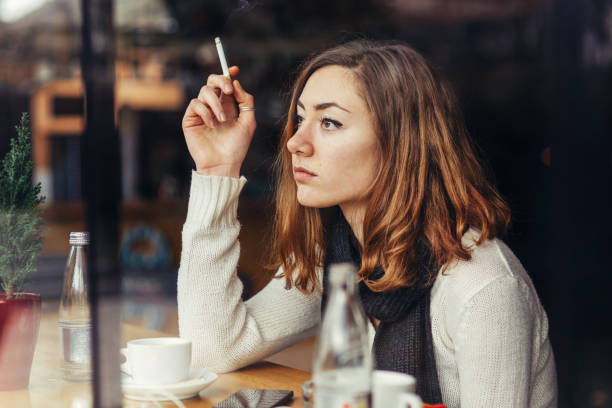 Coffee and cigarette Girl holding a burning cigarette, sitting in a café and looking out the window little girl smoking cigarette stock pictures, royalty-free photos & images