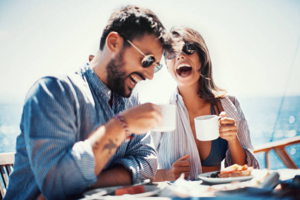 Coffee and fun on the sailing. Young couple laughing and drinking coffee at the sidewalk cafe on the beach. cruise vacation stock pictures, royalty-free photos & images