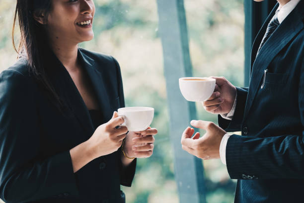 Coffee break. Group  business people, standing in modern office, holding a cups, smiling standing at the window stock photo