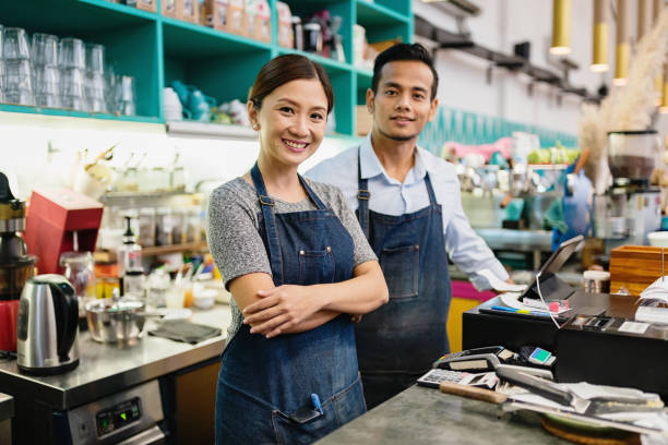 Coffee Shop Owner Couple Small Business Malaysia Proud, happy and confident smiling asian Small Business Coffee Shop Owner Couple standing together behind the counter in their stylish cafe in Kuala Lumpur, Malaysia business Malaysia stock pictures, royalty-free photos & images