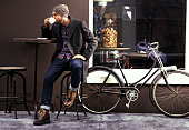 Shot of a handsome young man enjoying a cup of coffee at a cafe in the city while his bike stands next to him