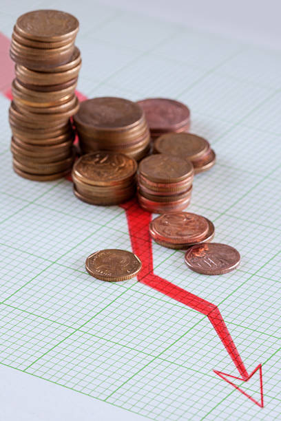 copper coins piled on graph paper showing a deline in earnings, with...