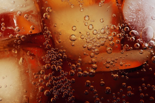 Macro shot of glass with cola drink and ice cubes.