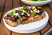 Cold appetizer of fried eggplant in a sweet sauce, decorated with fresh herbs with mozzarella cheese pieces, sprinkled with knjut seeds. The basis of the snack, a piece of fresh bread