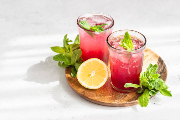 Cold sparkling hibiscus or karkade tea with lemon, mint and ice in glasses on a grey stone background. Summer drink, lemonade. stock photo