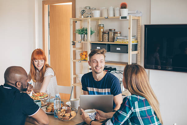 Coliving is new way of life Group of young people having breakfast at common kitchen. Checking their gadgets to catch up with latest news or messages. They are friends who sharing living space. roommate stock pictures, royalty-free photos & images