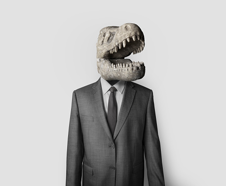 Collage image of man in dark suit with dinosaur skull instead of head. Obsolete thinking businessman against white background.Collage image of man in dark suit with dinosaur skull instead of head. Obsolete thinking businessman against white background.
