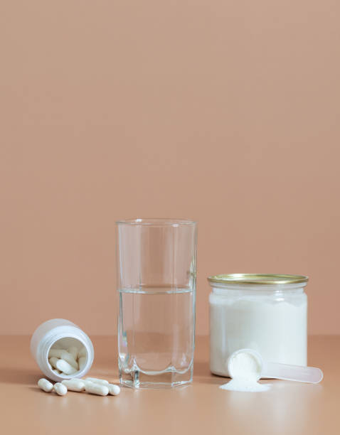 Collagen on a beige background. Collagen powder in a jar, pills and water close up. Protein intake. Vertical orientation. Copy space stock photo