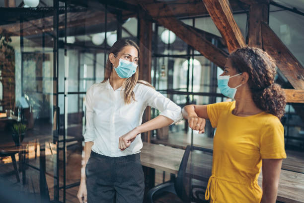 Colleagues greeting with an elbow bump in the office Businesswomen with protective masks meeting in the office elbow stock pictures, royalty-free photos & images