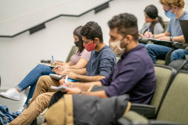 College Students wearing masks in a lecture hall College students sitting in a lecture hall on campus, all are wearing masks to protect from the transfer of germs. community colleges stock pictures, royalty-free photos & images