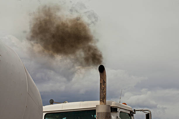 Color Image of Black Exhaust From a White Truck A white dump truck spews black exhaust smoke into a blue sky. Just the top of the truck is visible with the sky taking up half the image. The burning of fossil fuel by vehicles contributes to greenhouse gasses, pollution in urban city centers, and health concerns of people worldwide. exhaust pipe stock pictures, royalty-free photos & images