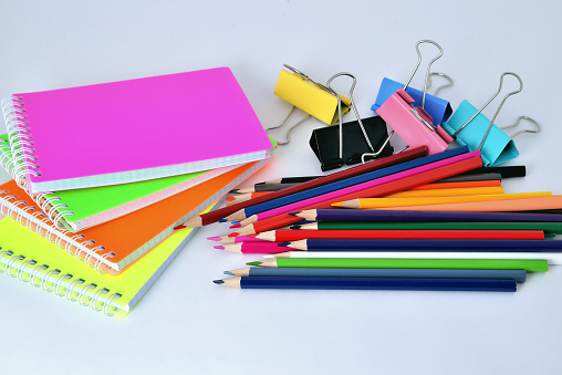 Color pads, pencils and paper clips on white background