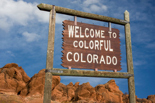 welcome to colorful Colorado roadside wooden sign with red sandstone cliff in background