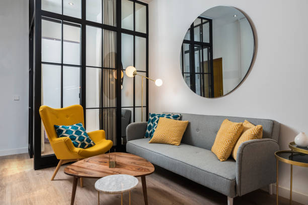 colorful and cozy living room with a designer armchair and sofa along with a round decorative mirror and glass wall. - artigo de decoração imagens e fotografias de stock