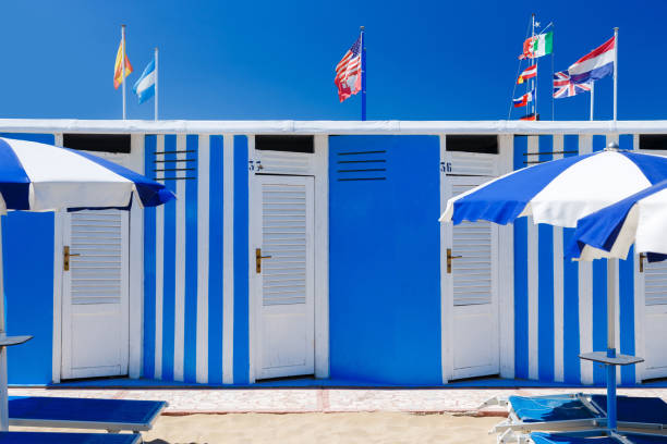 colorate capanne sulla spiaggia nella giornata estiva con cielo azzurro. bandiere sullo sfondo. - rimini foto e immagini stock