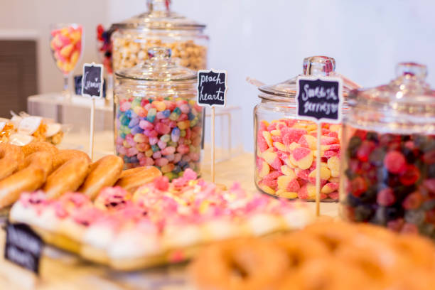 Colorful Candies in jars on a dessert table with donuts, cookies and popcorn. There are cute chalkboard signs. Colorful Candies in jars on a dessert table with donuts, cookies, and popcorn. There are cute chalkboard signs. candy jar stock pictures, royalty-free photos & images