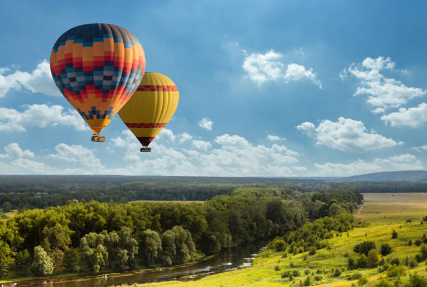 Colorful hot air balloon flying over green field Colorful hot air balloon flying over green field and river basket photos stock pictures, royalty-free photos & images