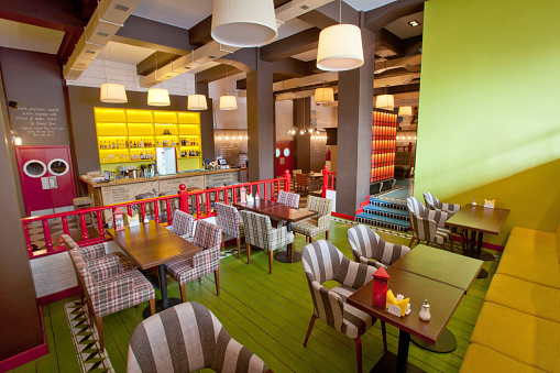 Ornamental chairs and tables located in stylish cafeteria with colorful walls and modern lamps