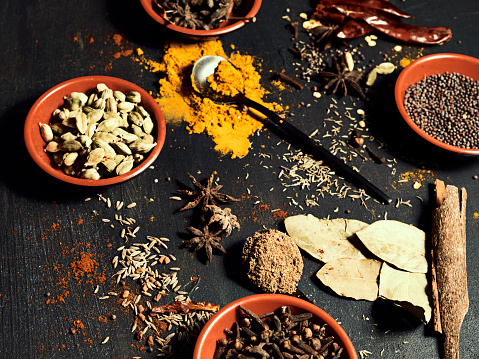 Colorful kitchen ingredients, herbs and spices covering a wood table. Closeup view of messy natural stock after being used for preparing and cooking food. Indian curry consumables on a home counter