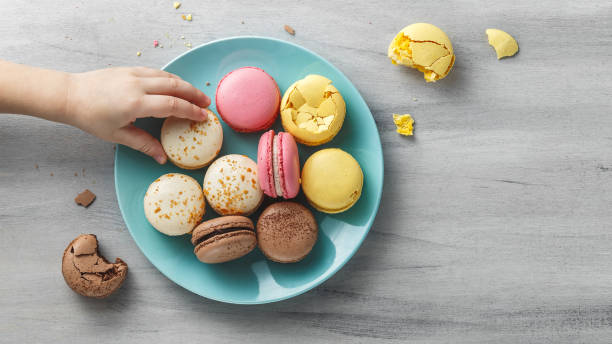 Colorful macaroons on a plate on a wooden table Little, kid's hand reaching for a macaroon from a turquoise plate on a wooden textured table. Copy space sugar food stock pictures, royalty-free photos & images