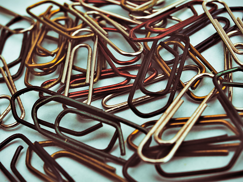 Colorful paperclips on light blue background. Old photo effect.
