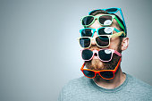 A portrait of a man with a large beard, wearing multiple pairs of multi-colored sunglasses.  Studio shot; horizontal with copy space.