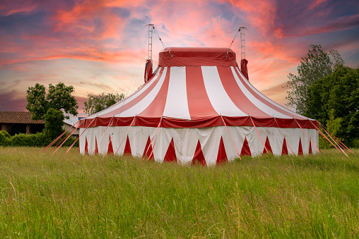 Colourful circus tent on green meadow against a colorful sunset sky