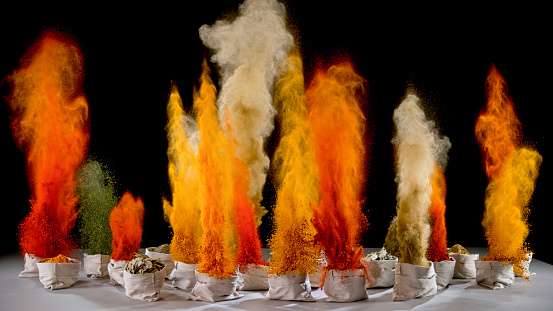 Vibrant spices exploding into air from bags on black background.