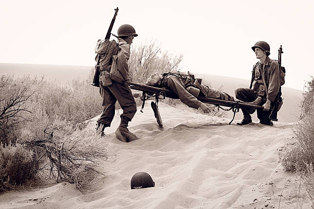 WW2 Combat Zone A World War 2 American army soldier in the desert is shot and wounded by the enemy. Two of his comrades carry him away on a stretcher. Part 3 of combat action sequence. Authentic WW2 army uniforms. Vintage black and white photojournalism style. More vintage military photos. conflict photos stock pictures, royalty-free photos & images