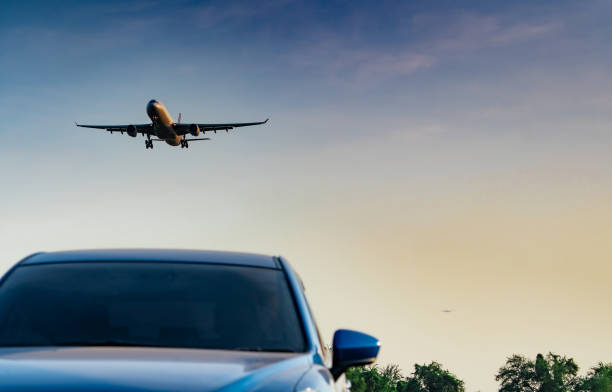 Commercial airline. Passenger plane landing approach blue SUV car at airport with blue sky and clouds at sunset. Arrival flight. Vacation time. Happy trip. Airplane flying on bright sky. Car parked. stock photo