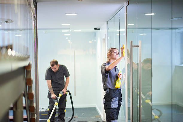 commercial deep clean a female cleaning contractor is polishing the glass partition offices whilst In the background a male colleague steam cleans an office carpet in a empty office in between tenants. . Office cleaning stock pictures, royalty-free photos & images