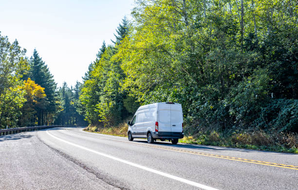 Compact cargo commercial mini van driving on the turning road with forest on the sides stock photo
