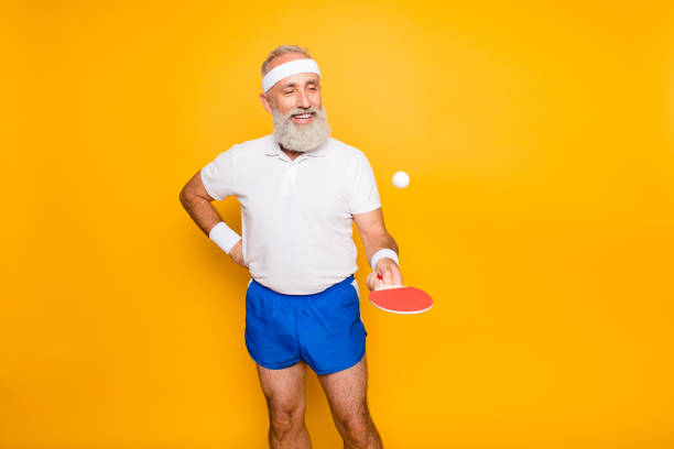Competetive emotional cool active comic grandpa with beaming grin, with table tennis equipment. Healthcare, weight loss, bodycare lifestyle, wearing blue sexy shorts, so hot! Competetive emotional cool active comic grandpa with beaming grin, with table tennis equipment. Healthcare, weight loss, bodycare lifestyle, wearing blue sexy shorts, so hot! table tennis stock pictures, royalty-free photos & images